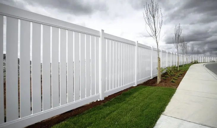 A white fence with grass and trees in the background