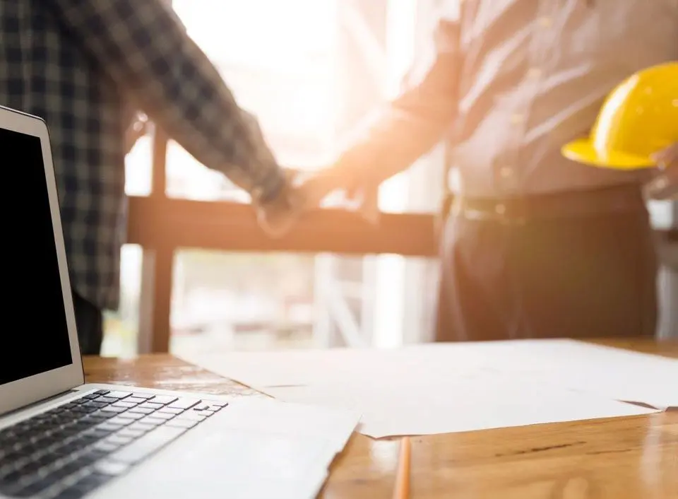 Two people shaking hands over a laptop.