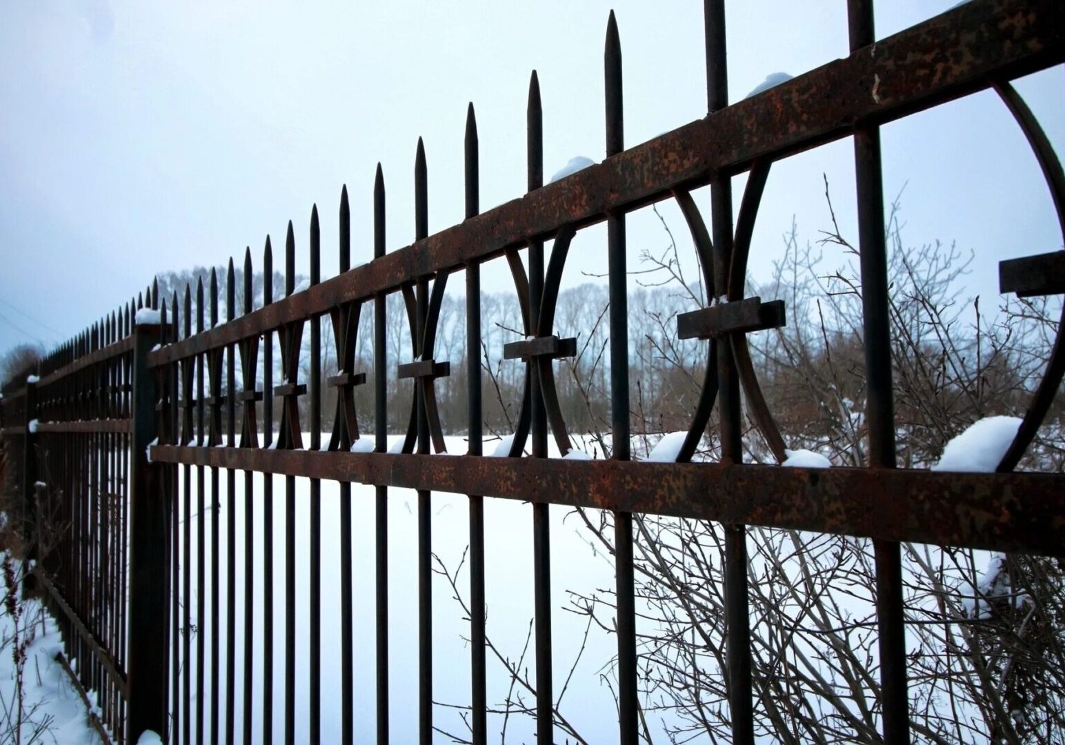 A fence with metal bars and snow on the ground.